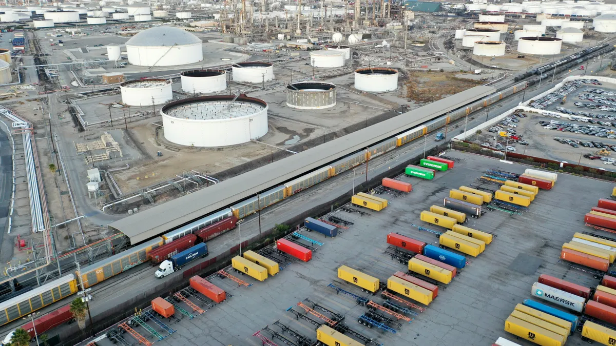 In an aerial view, a freight rail car (C) passes near shipping containers on November 22, 2022 in Wilmington, California.