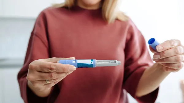 A person holds a GLP-1 injection drug with the cap off.