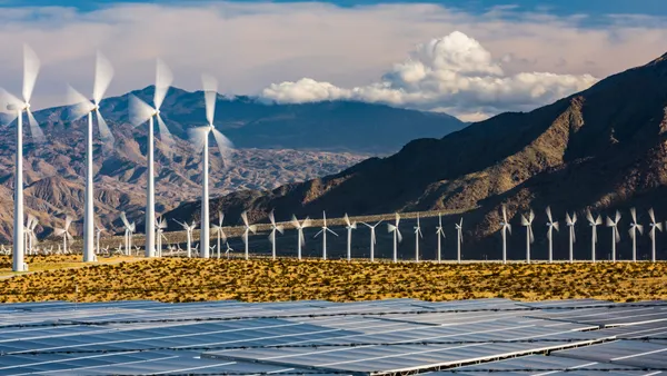 Wind turbines spin with solar panels in the foreground.