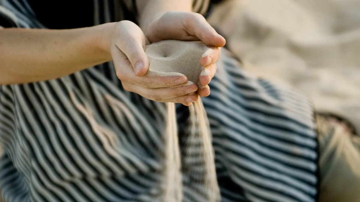 Sand slipping through hands cupped together.