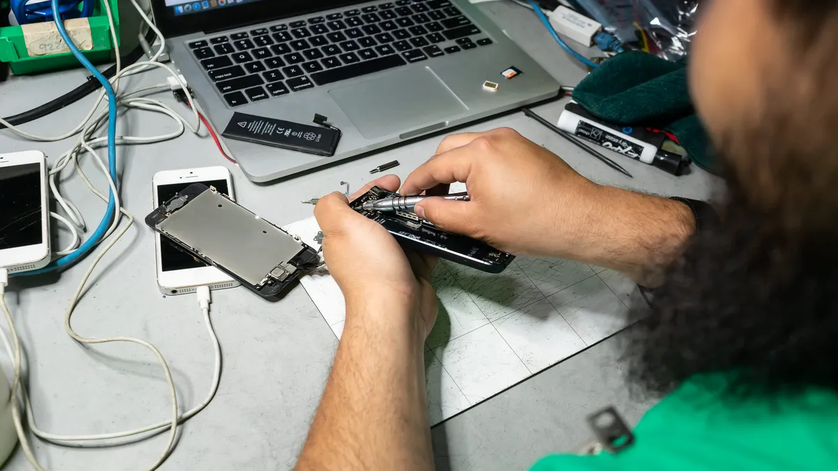 A close-up of an employee using tools to repair a cell phone in a warehouse.