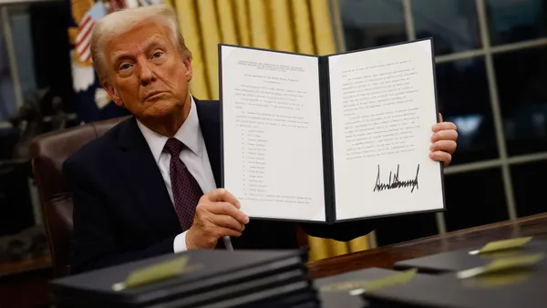 Donald Trump holds up a signed executive order while sitting at his desk in the Oval Office