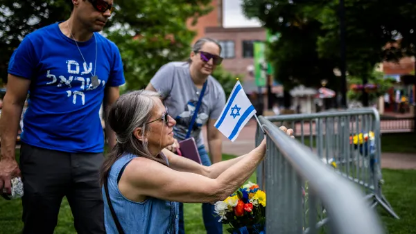 A person attaches a white flag with a blue star onto a barricade fence while two other people look on.