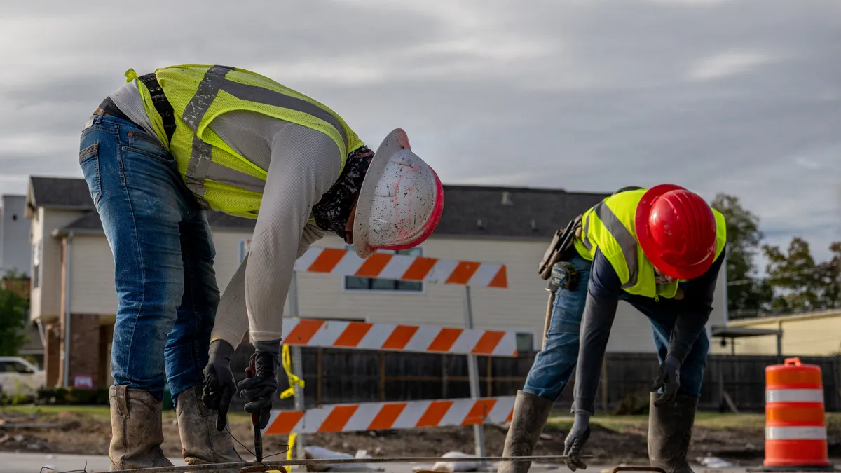 Two construction workers bend over to perform work.