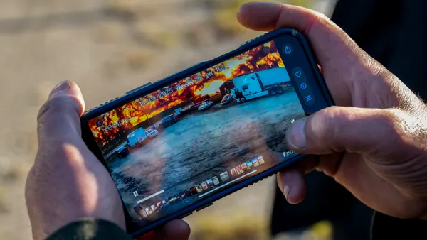 Hands hold a phone showing a video with vehicles in the foreground and a blazing fire in the background.