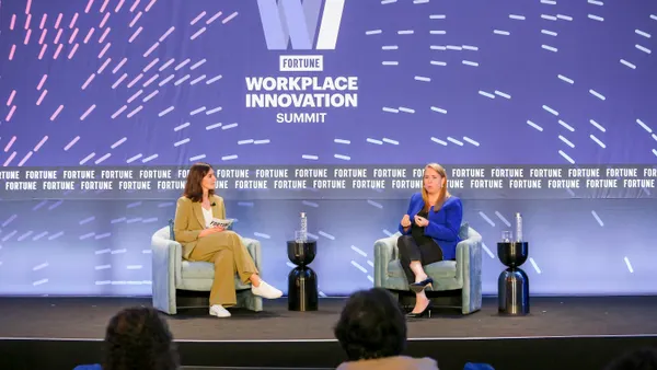 Two women in business clothes sit on a stage and have a conversation in front of a "Fortune Workplace Innovation Summit" sign.
