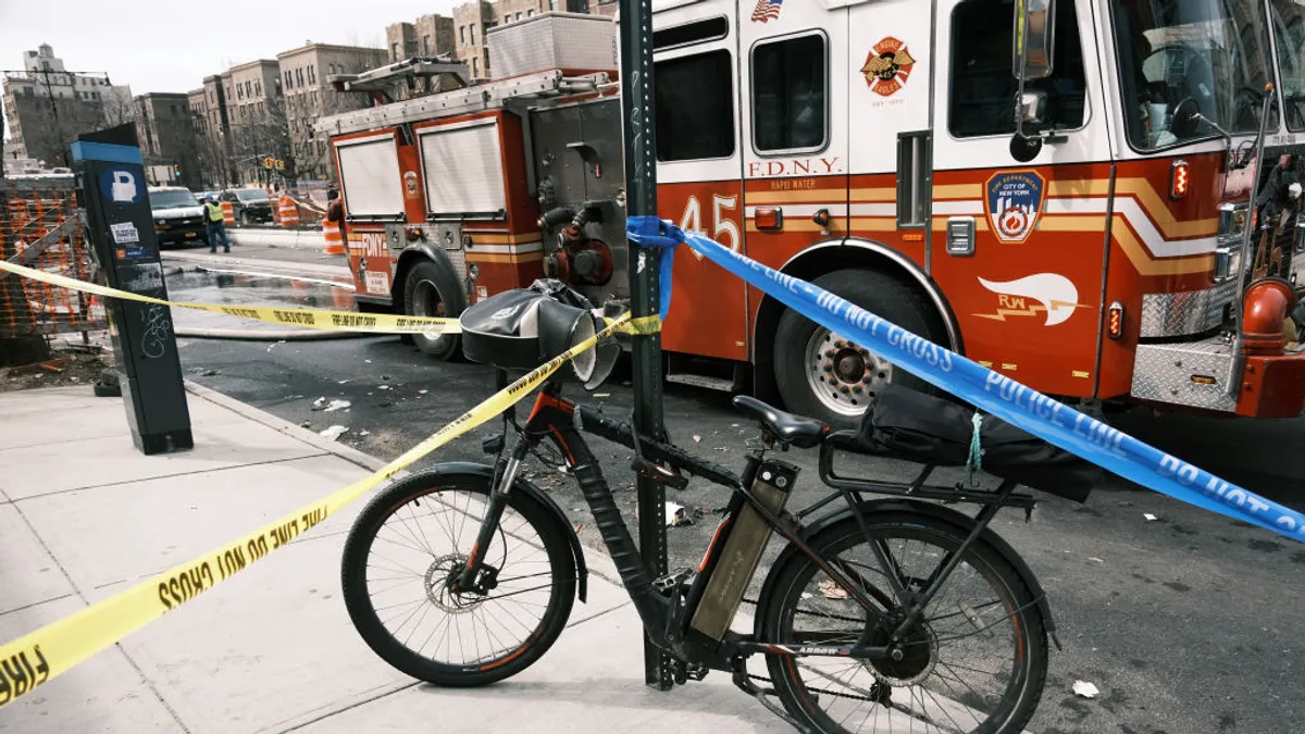 An electric bike is locked to a street sign in front of a red fire truck, with caution type surrounding it