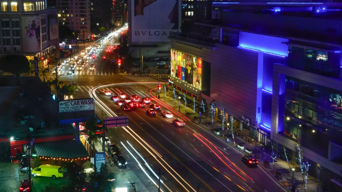 Cars at night with streaks of headlights and tail lights on a wide street with building on each side.