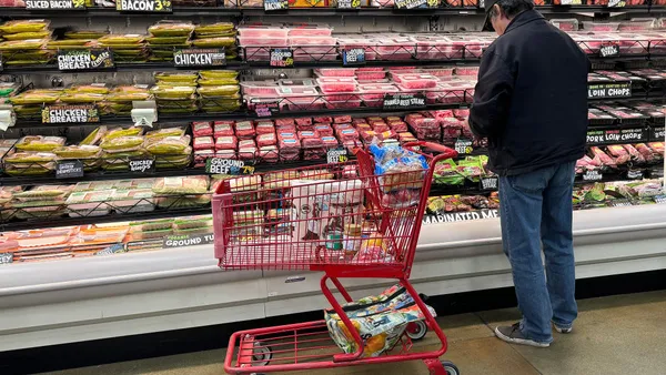 A man stands with a shopping cart in front of a grocery store meat aisle