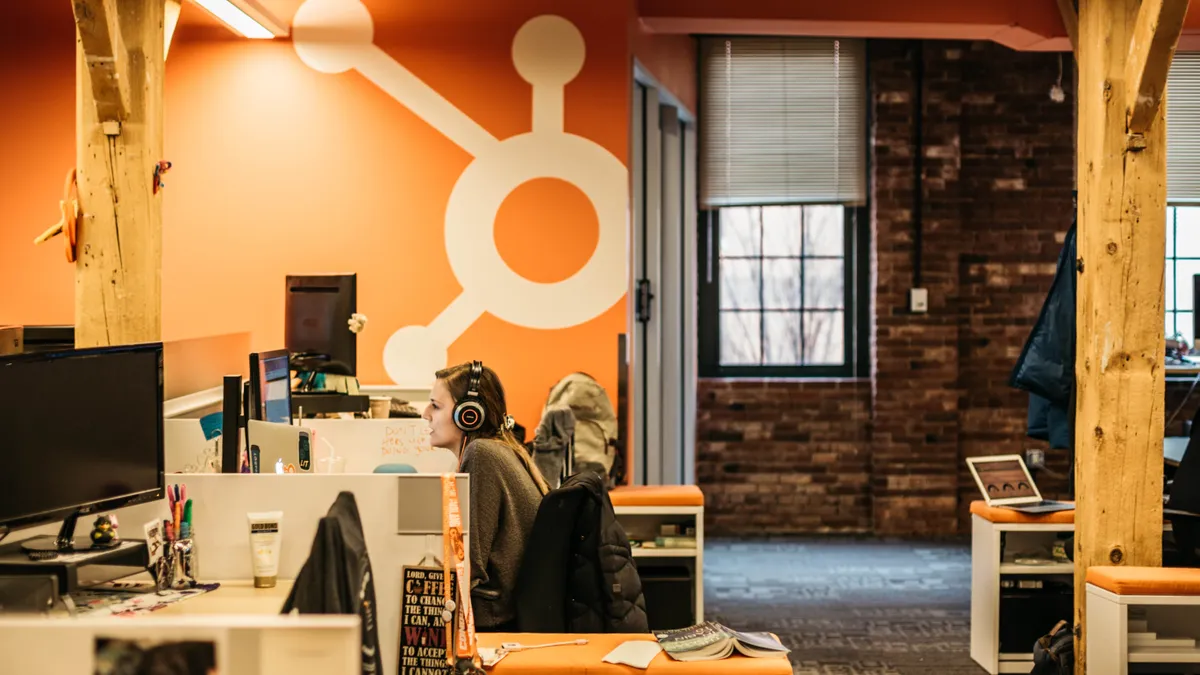 Person works in an office with an orange wall behind depicting a view of the Hubspot logo