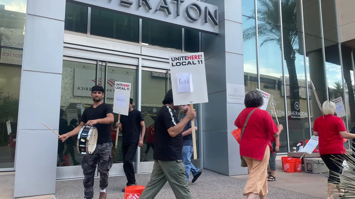 Workers hold picket signs and a drum as they march in a circle.