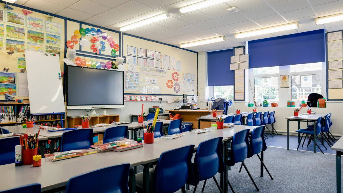 A school classroom with chairs and desks facing a blackboard at the front of the room.