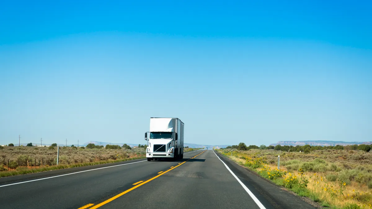 A truck on Route 66 travels by an open field with a blue sky in the background.