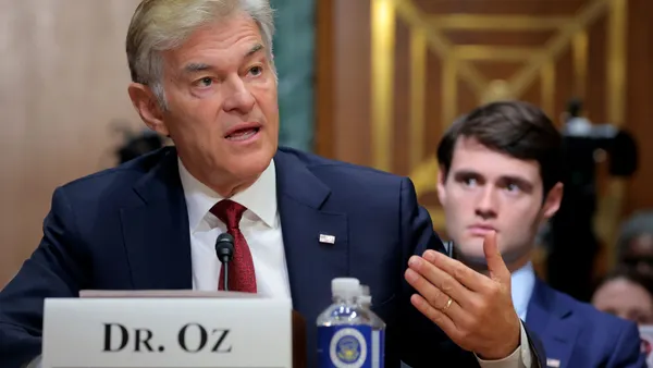 Dr. Mehmet Oz sits on a table in front of a namecard bearing his name.