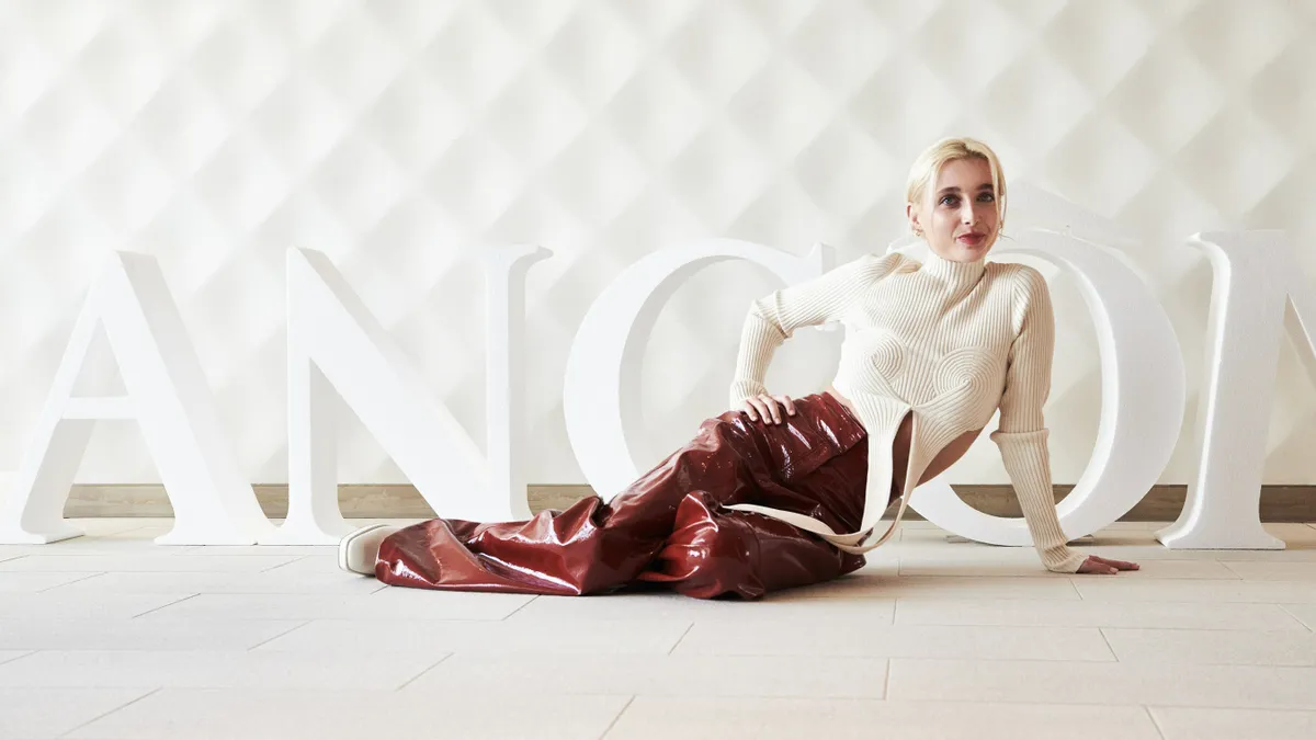 Emma Chamberlain lays on her side in front of a Lancome sign.