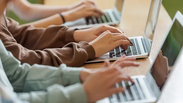 Three people's arms and hands are pictured using three laptops sitting on a table