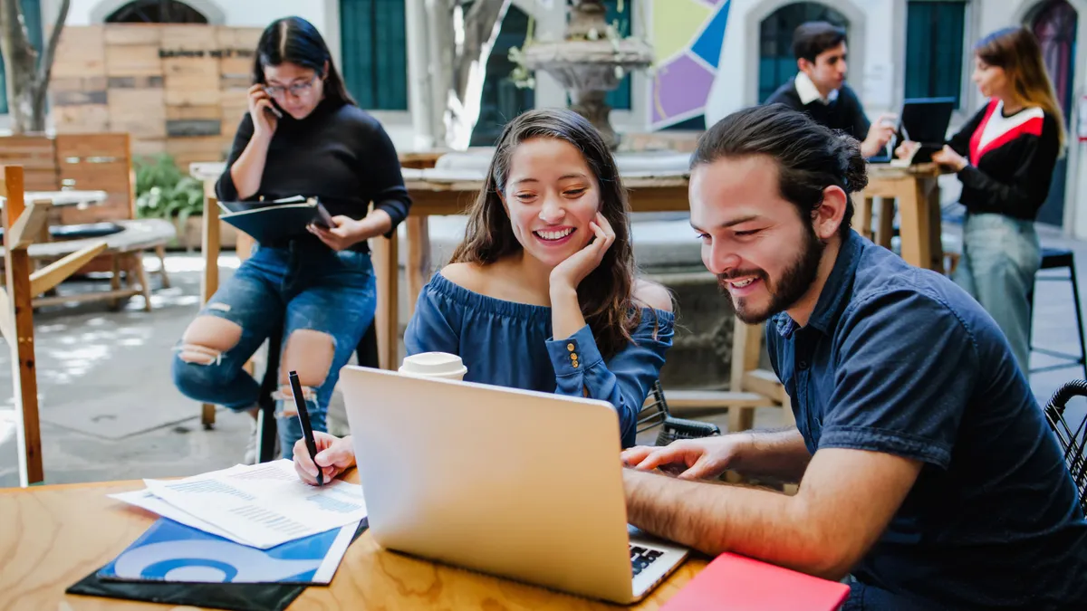 two people sitting at a table looking at a laptop