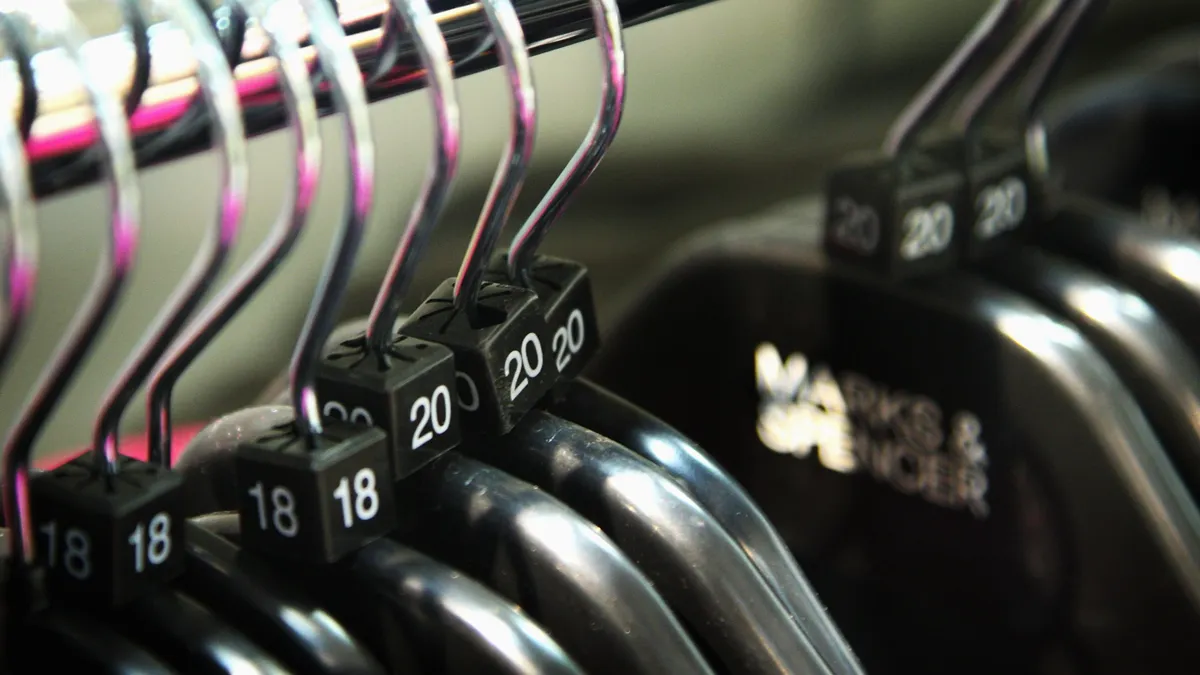 A row of black hangers hang on a silver clothes rod with the numbers 18 and 20 on the hanger necks.