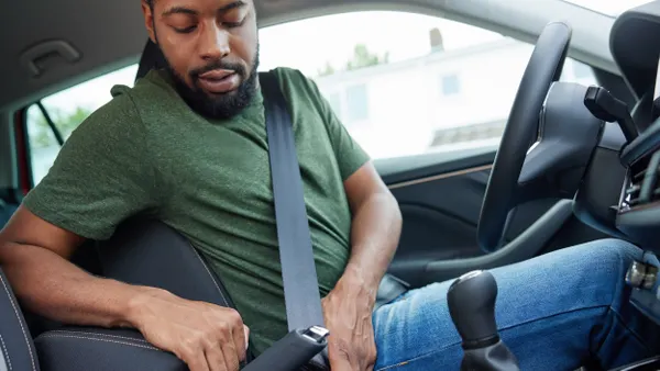 A man seated in the driver's seat of a car buckling his lap and shoulder belt.