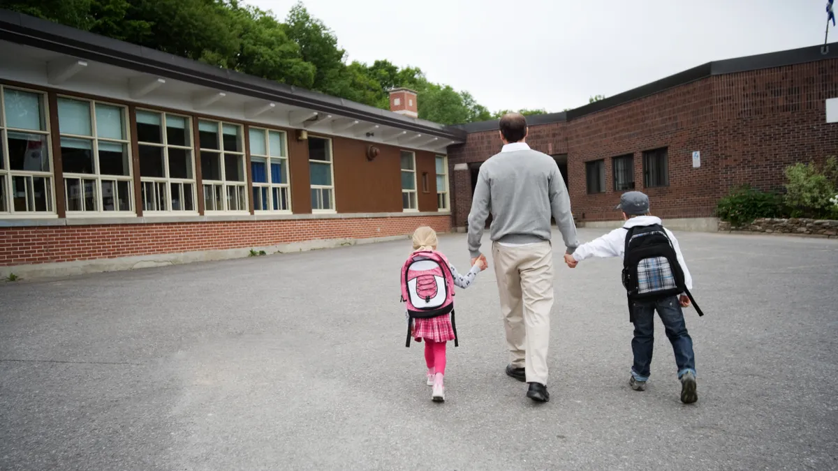 A parent walks two students to school outside of the building.