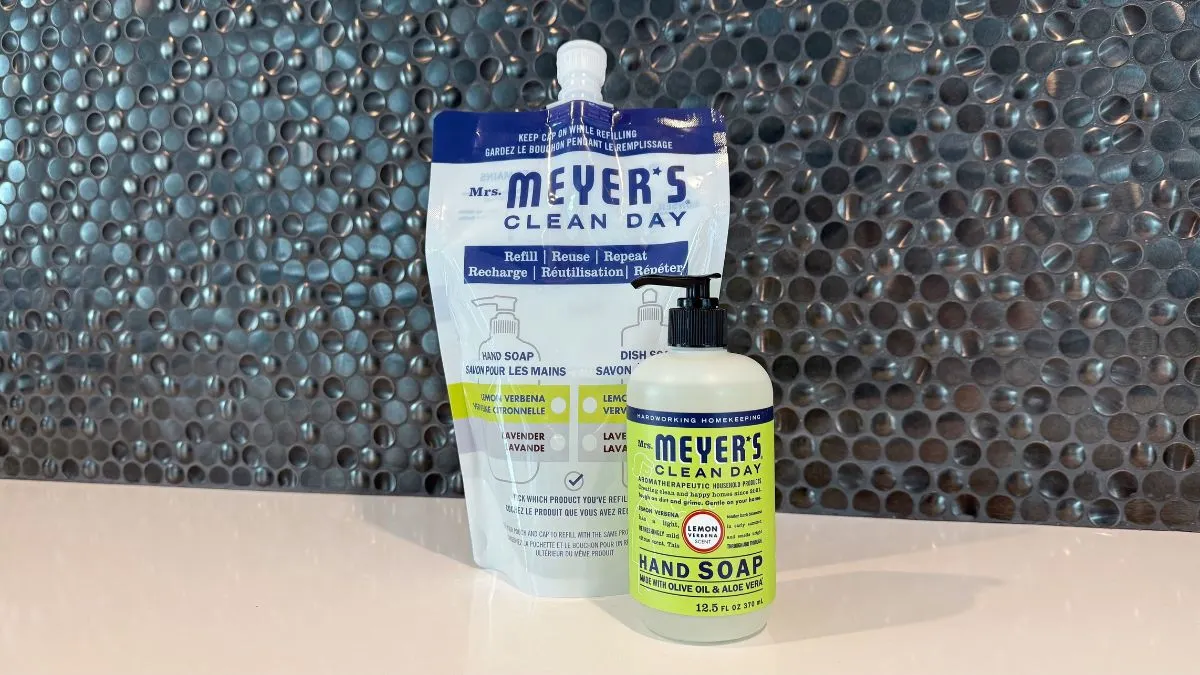 A rigid plastic bottle of Mrs. Meyer's liquid hand soap sits next to a larger, flexible plastic pouch of the same product.
