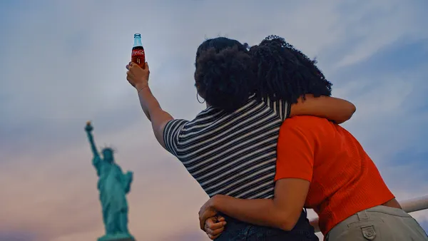 Two people with a Coca-Cola bottle in front of the Statue of Liberty