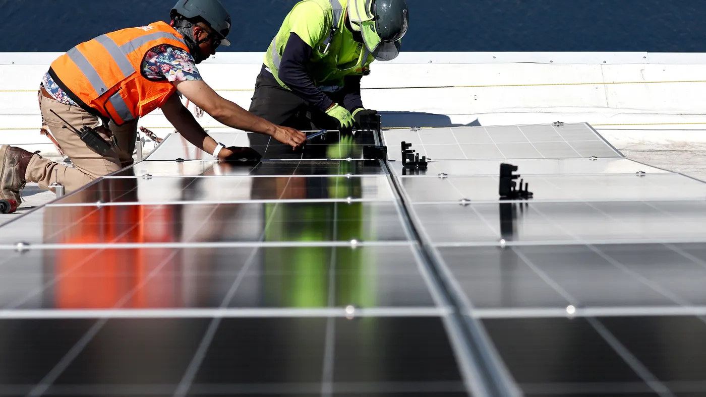 Two men install solar panels on a roof.