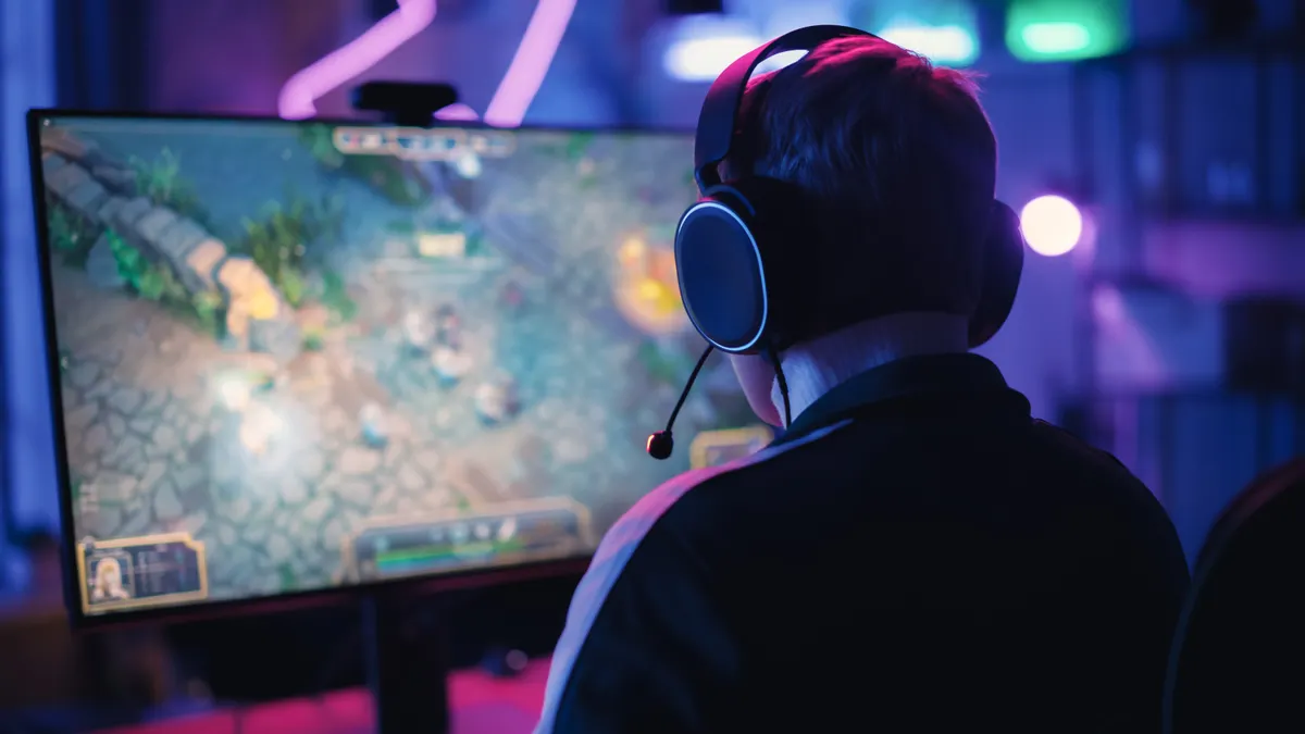 Over the shoulder angle of a young gamer playing a video game on personal computer in a neon lit living room at home.