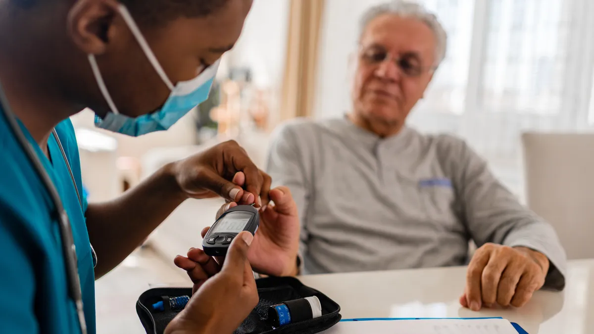 A visiting nurse helps a patient at home with CGM monitoring