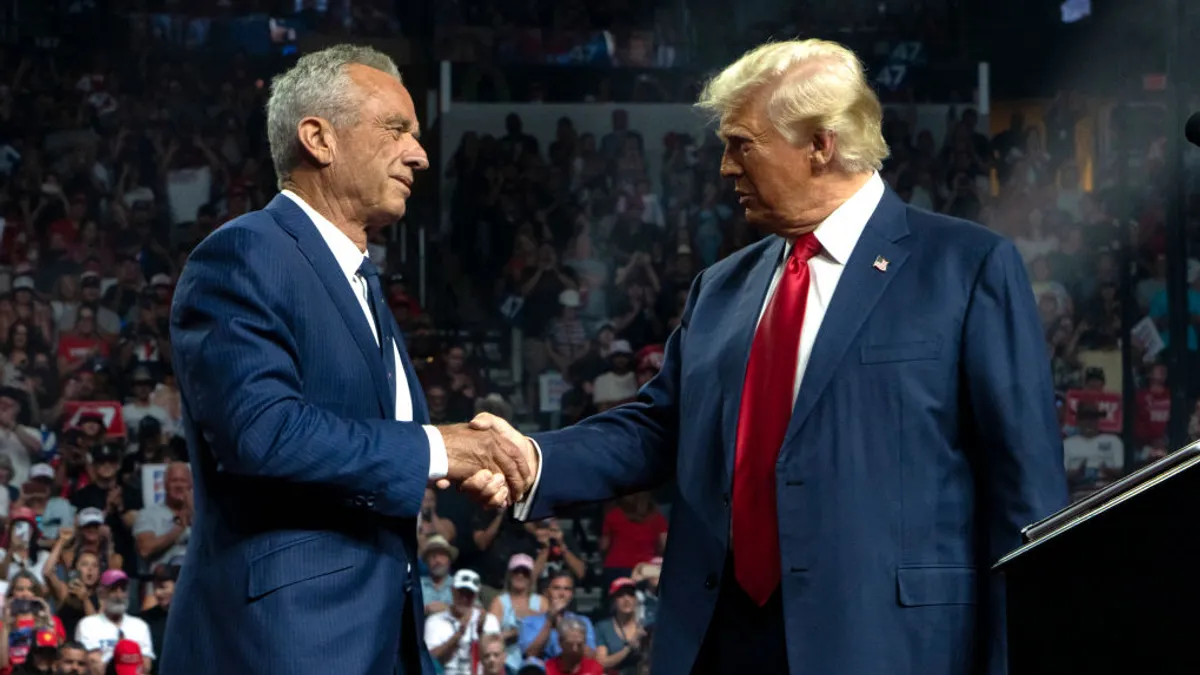 RFK Jr. shakes hands with Donald trump on stage with a crowd behind watching