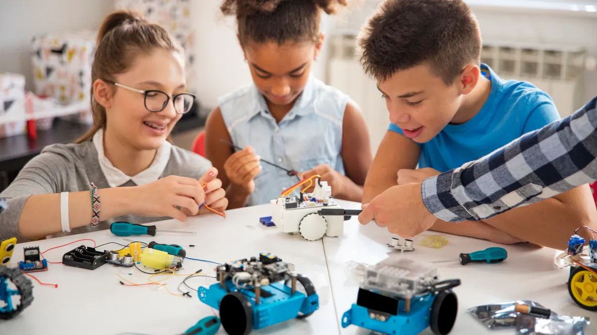 Three juvenile students work on a robot design project at a table in a classroom.