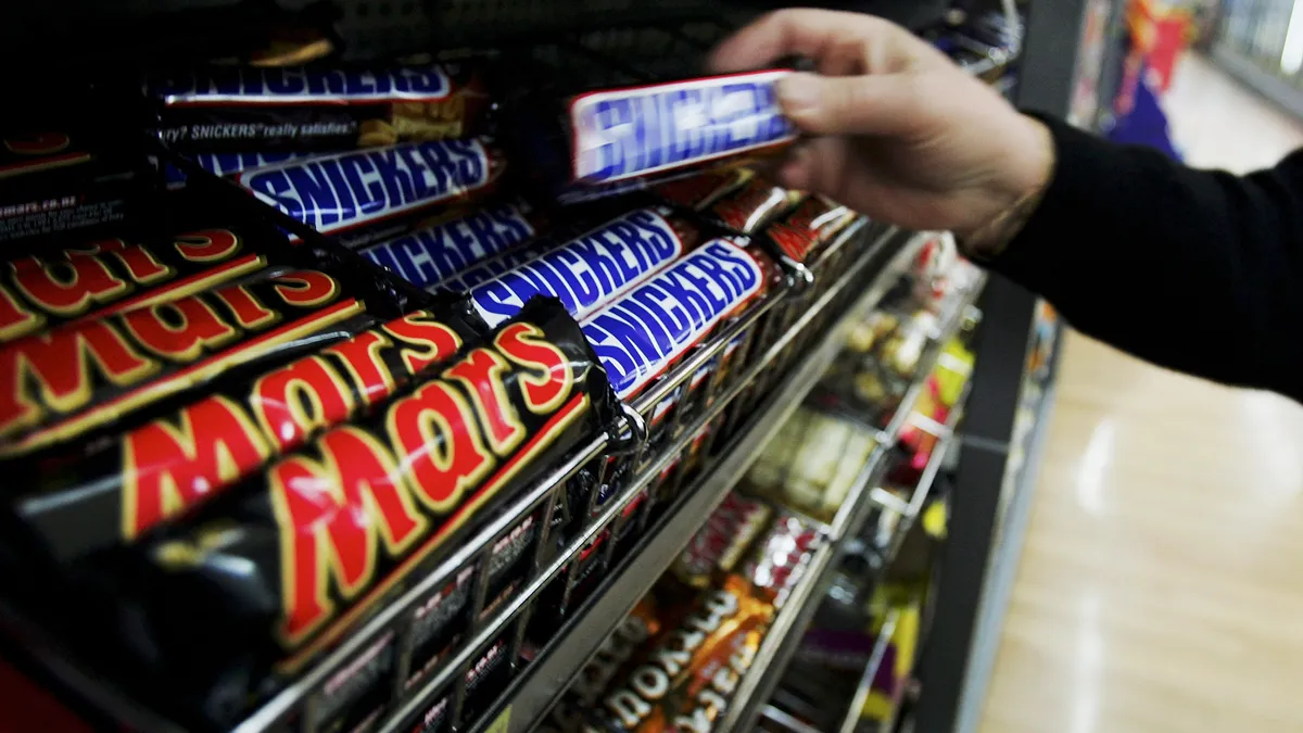 A consumer reaches for a Snickers bar in a store.