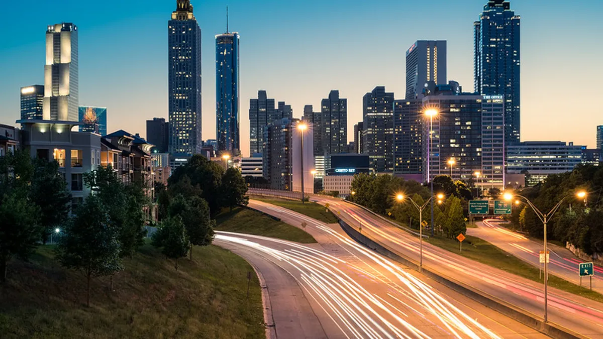 A nighttime view of a city skyline, with streaks of light from the highway in the foreground.