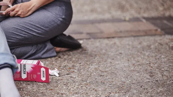 A woman sitting on the ground, focused on her cell phone, with a relaxed posture and a thoughtful expression.