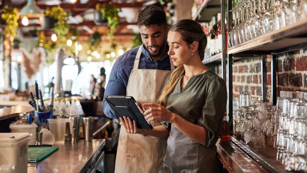 Two people looking at a digital tablet behind a bar