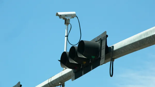 A traffic signal mounted horizontally on an overhead arm next to a camera.