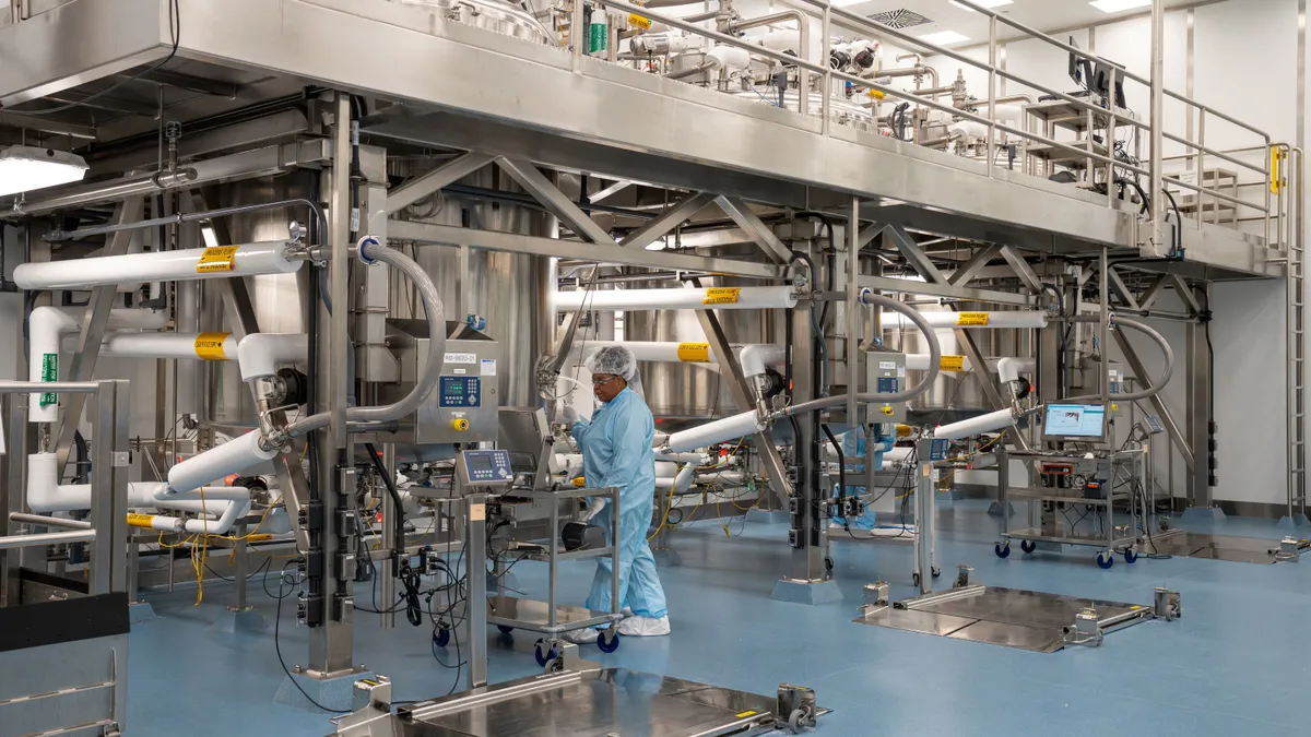 A woman in scrubs standing next to manufacturing equipment in a large room filled with scientific steel equipment