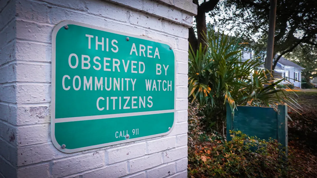 a neighborhood watch sign on a white brick wall