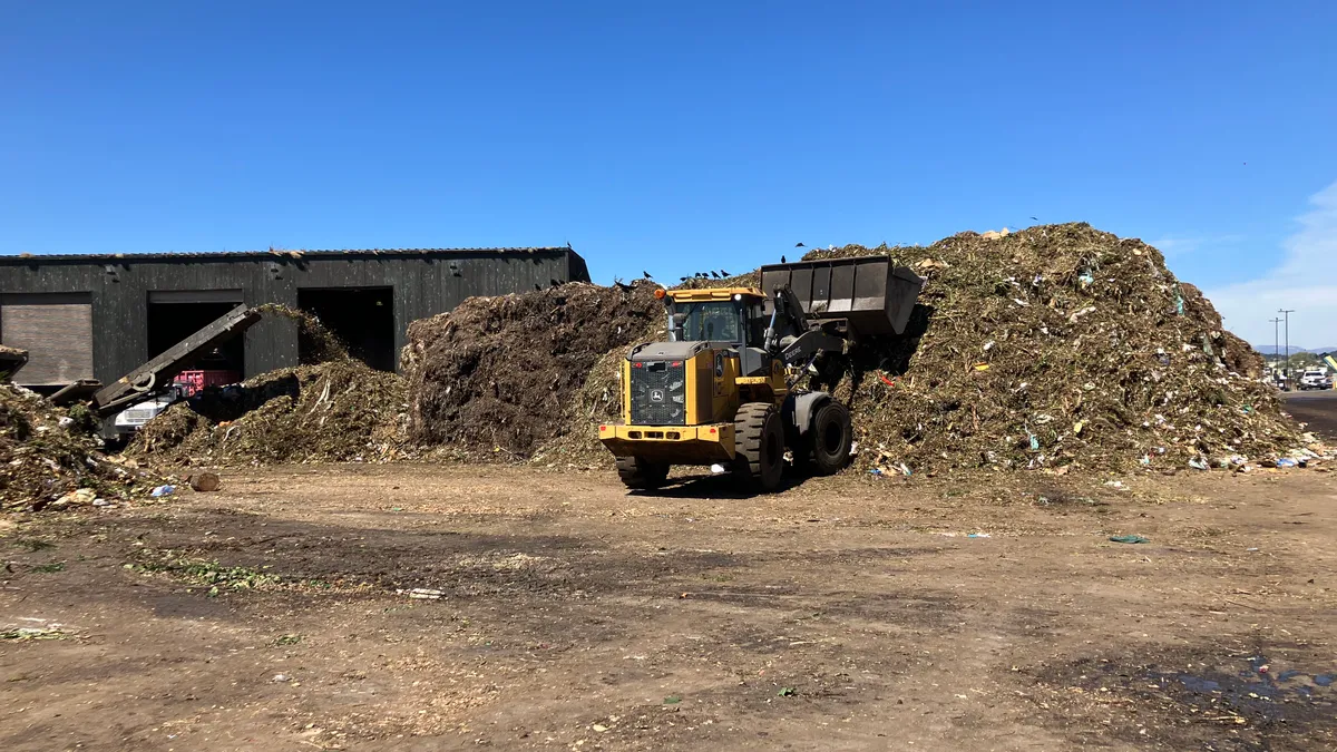 Piles of organic material in the composting process, managed by a piece of heavy equipment