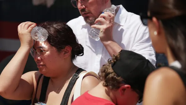 A person holds a plastic water bottle to their forehead ,and another person holds a plastic water bottle to their cheek.