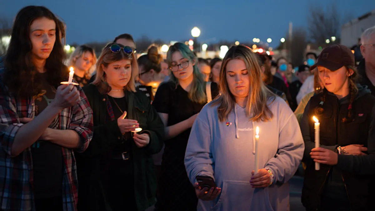 People stand outside holding candles during a vigil.