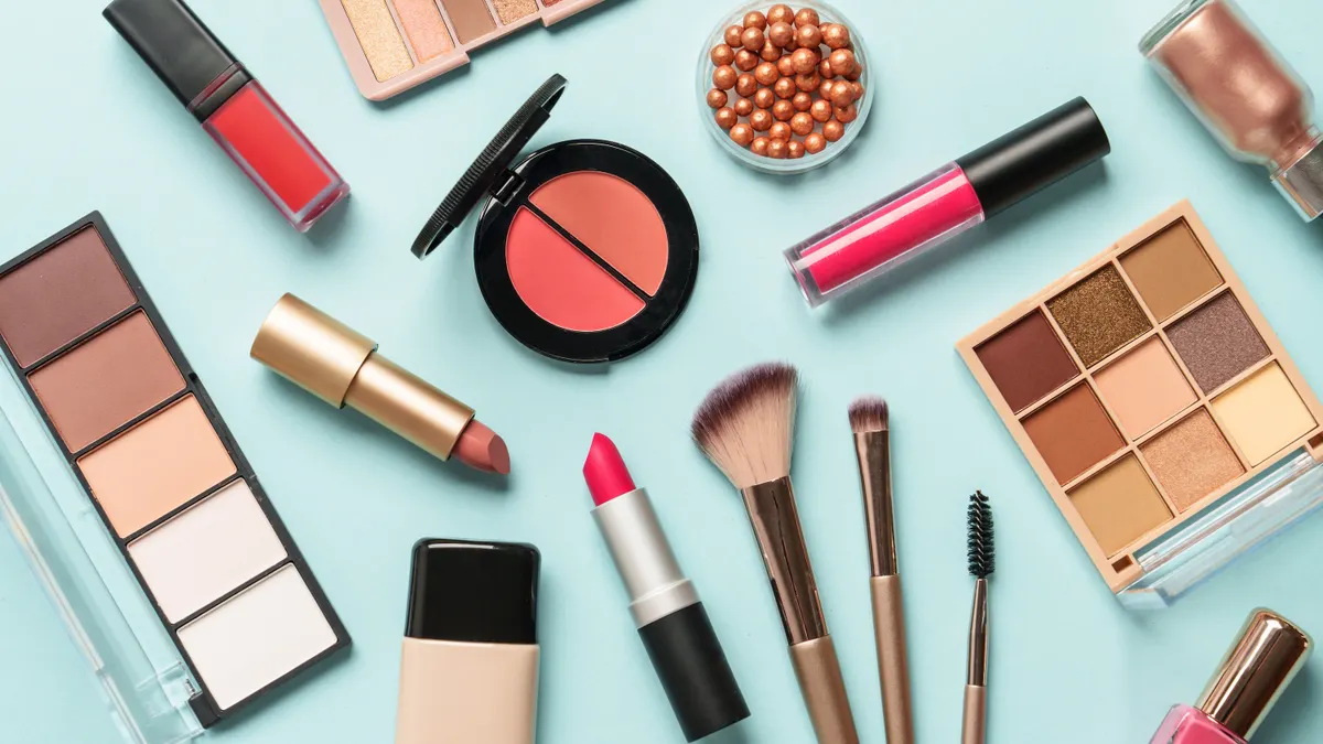 Skin tone palette, lipsticks, makeup brushes, eyeshadow palettes and nail polish on a sky blue background.