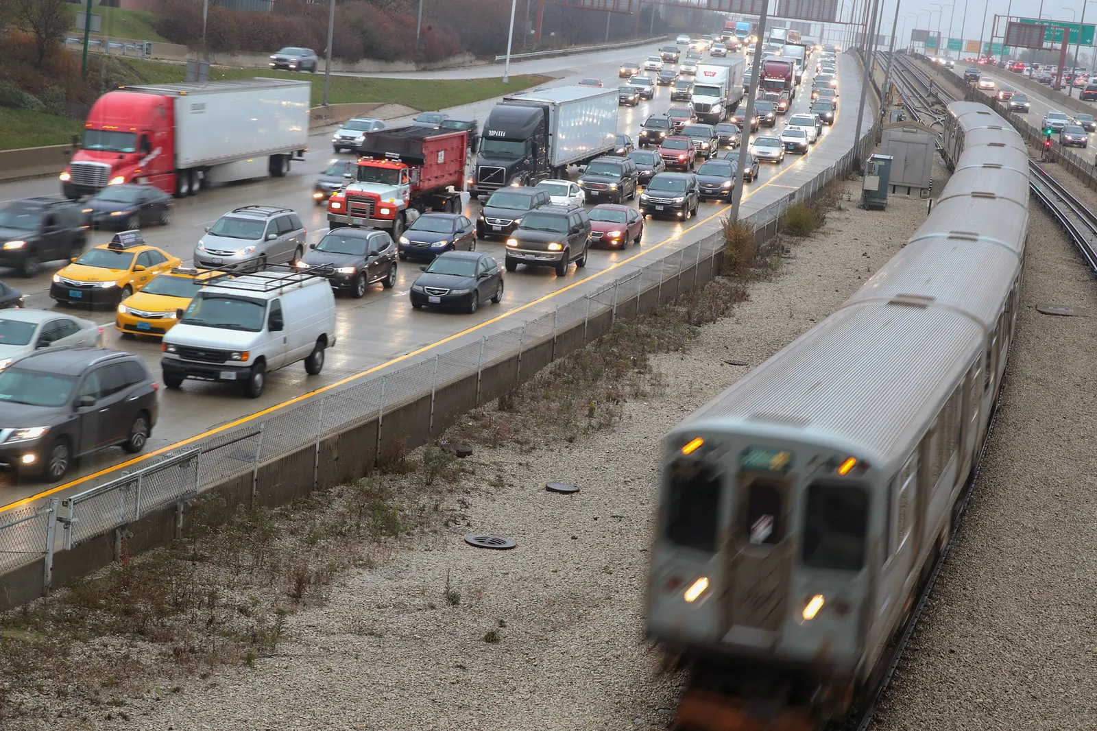 Many cars are bumper to bumper on a highway; to the right, a subway train is passing.