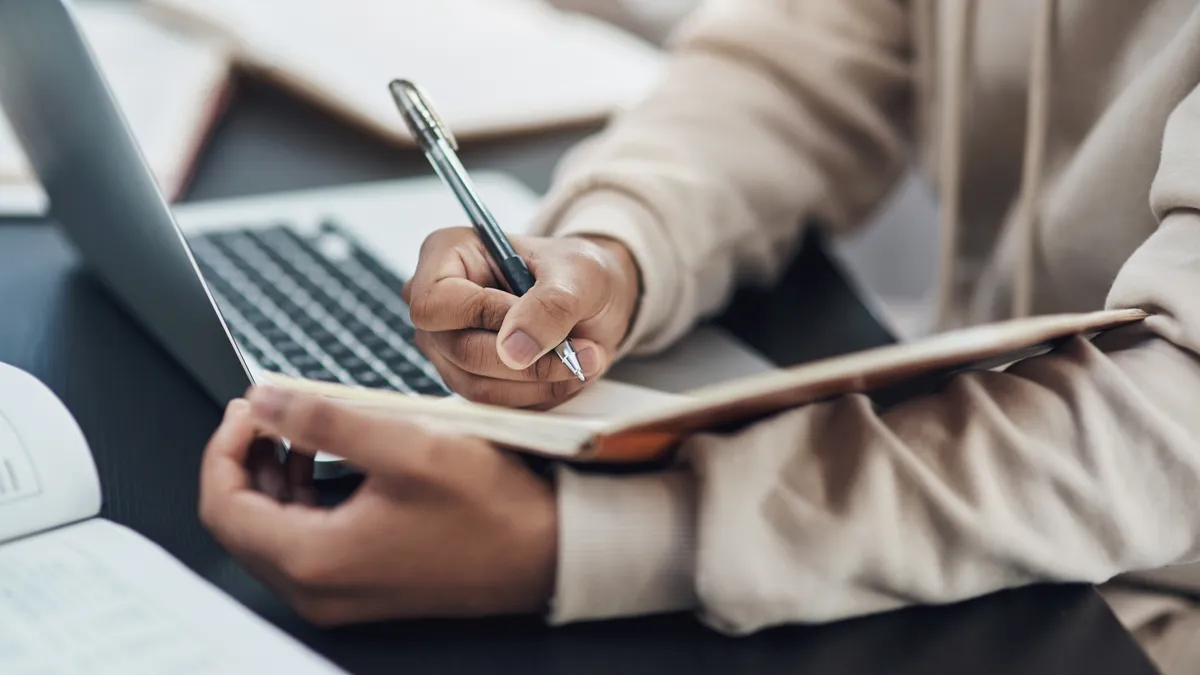 Shot of an unrecognisable man writing in a notebook while working from home