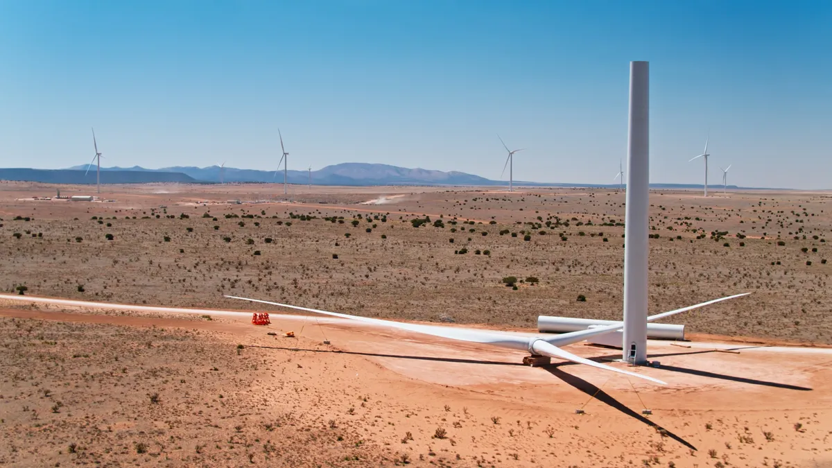 An incomplete wind turbine rises from the New Mexico desert, with several completed ones behind it.