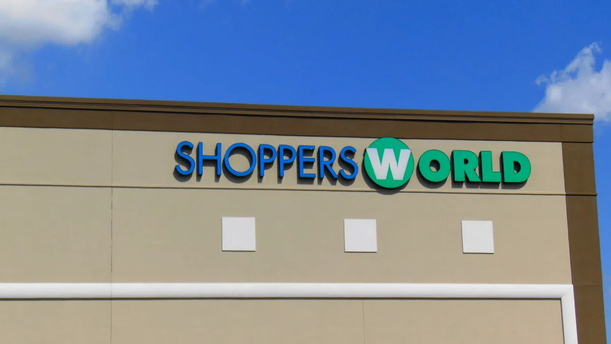 White puffy clouds in a bright blue sky float over a cream-colored building with the words "Shoppers World."