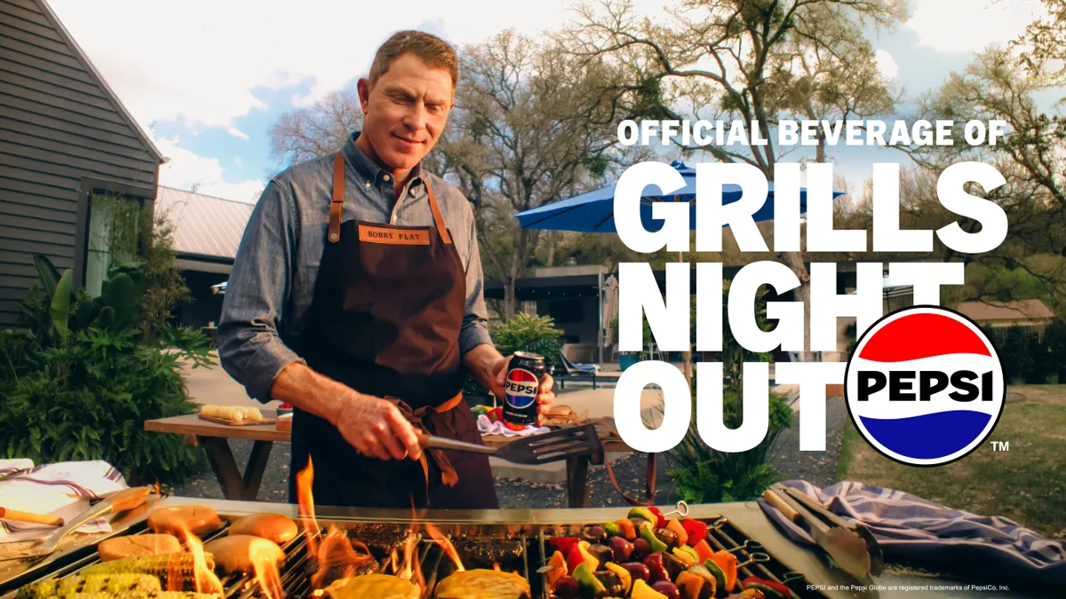 Celebrity chef Bobby Flay, wearing an apron, stands behind a grill outside and prepares dishes in a Pepsi ad