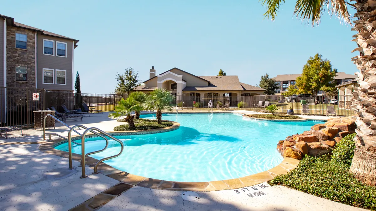 Pool with brown apartments to the left and a clubhouse in the back.