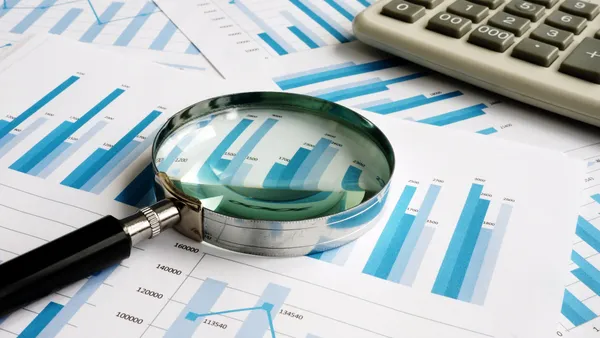 Papers with bar graphs all over a flat surface with a calculator and magnifying glass on top of them.