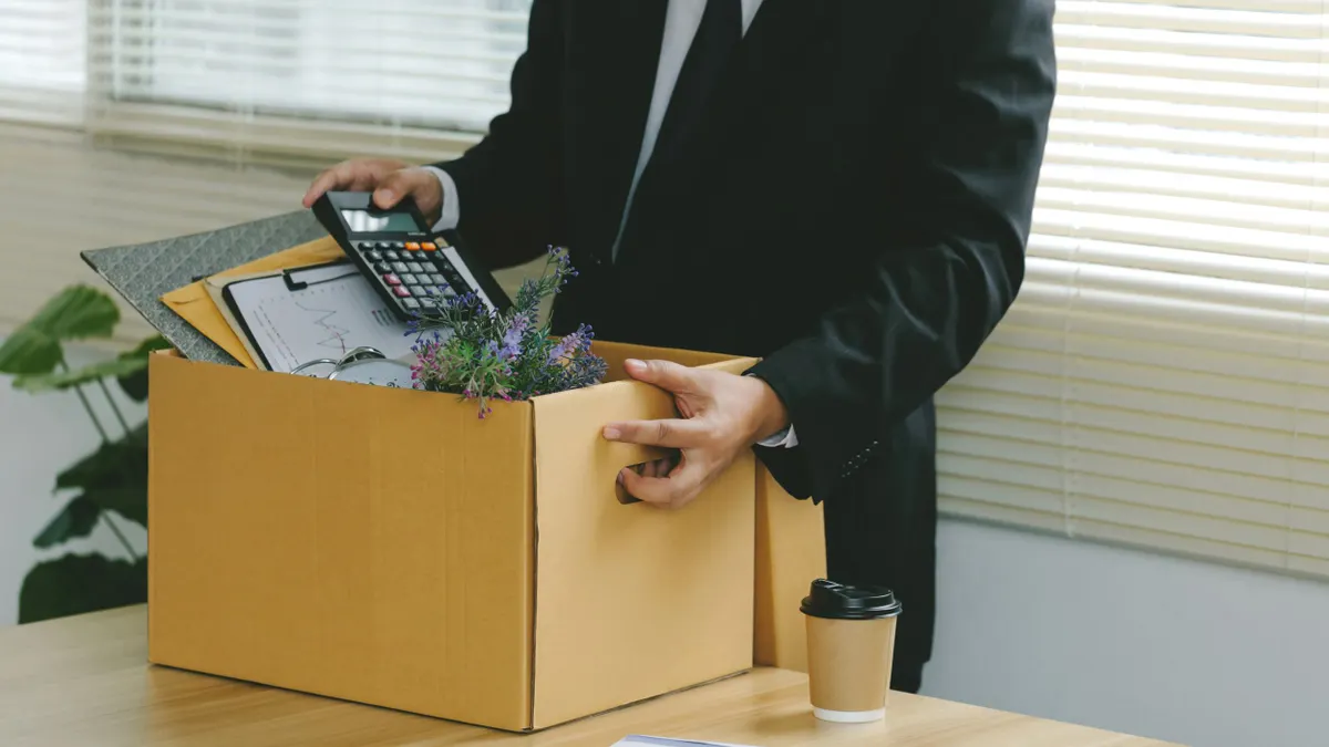 Businessman carries cardboard with office supplies.